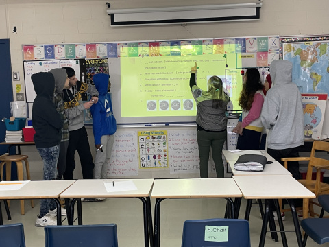 Junior high students and teacher learning at a white board in a classroom