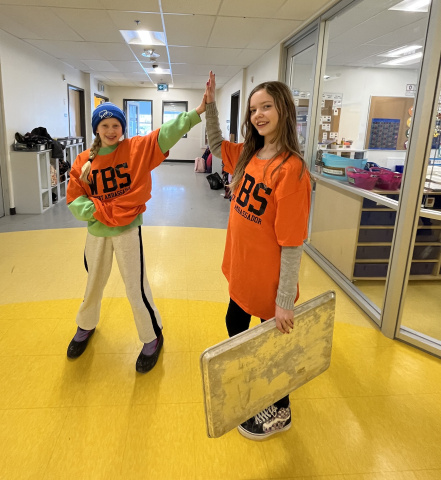 Photo shows two student ambassadors in orange shirts giving each other a high five in the hall at West Bedford School as they deliver lunch.